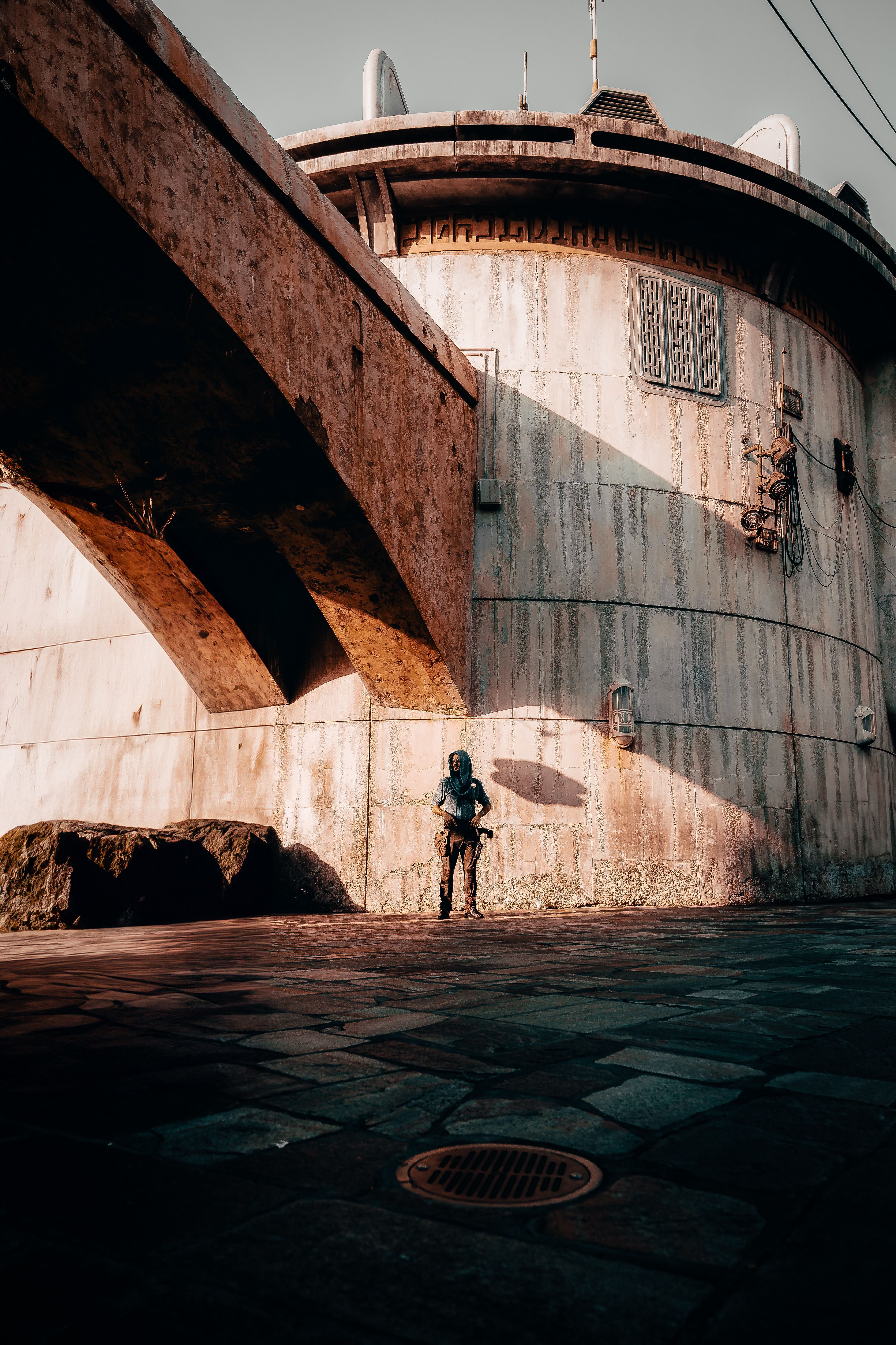 Moody urban scene featuring a rusty overhead bridge and a solitary figure in shadow.