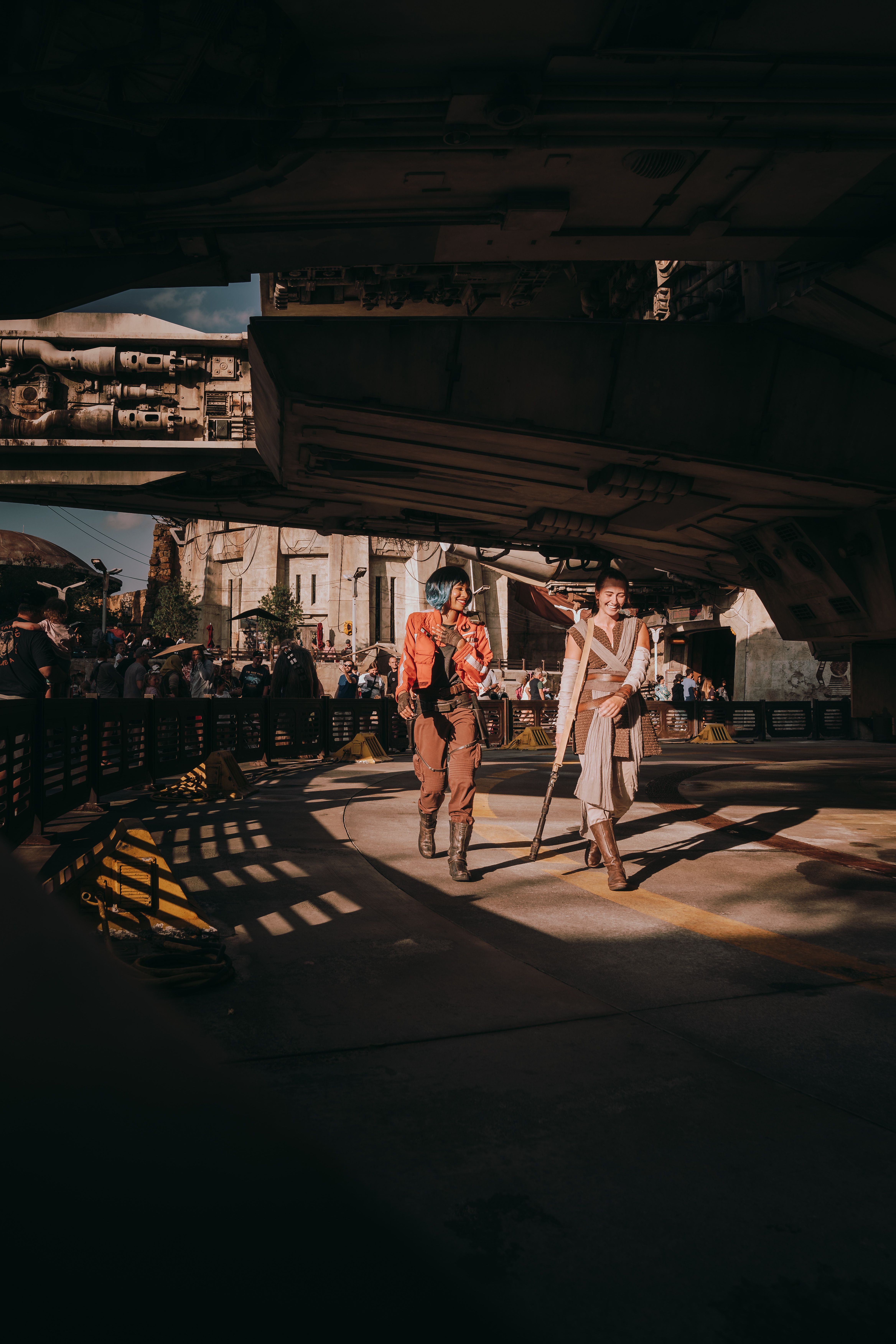 Cosplayers dressed as characters from a sci-fi universe walk under a fictional spaceship in a theme park.