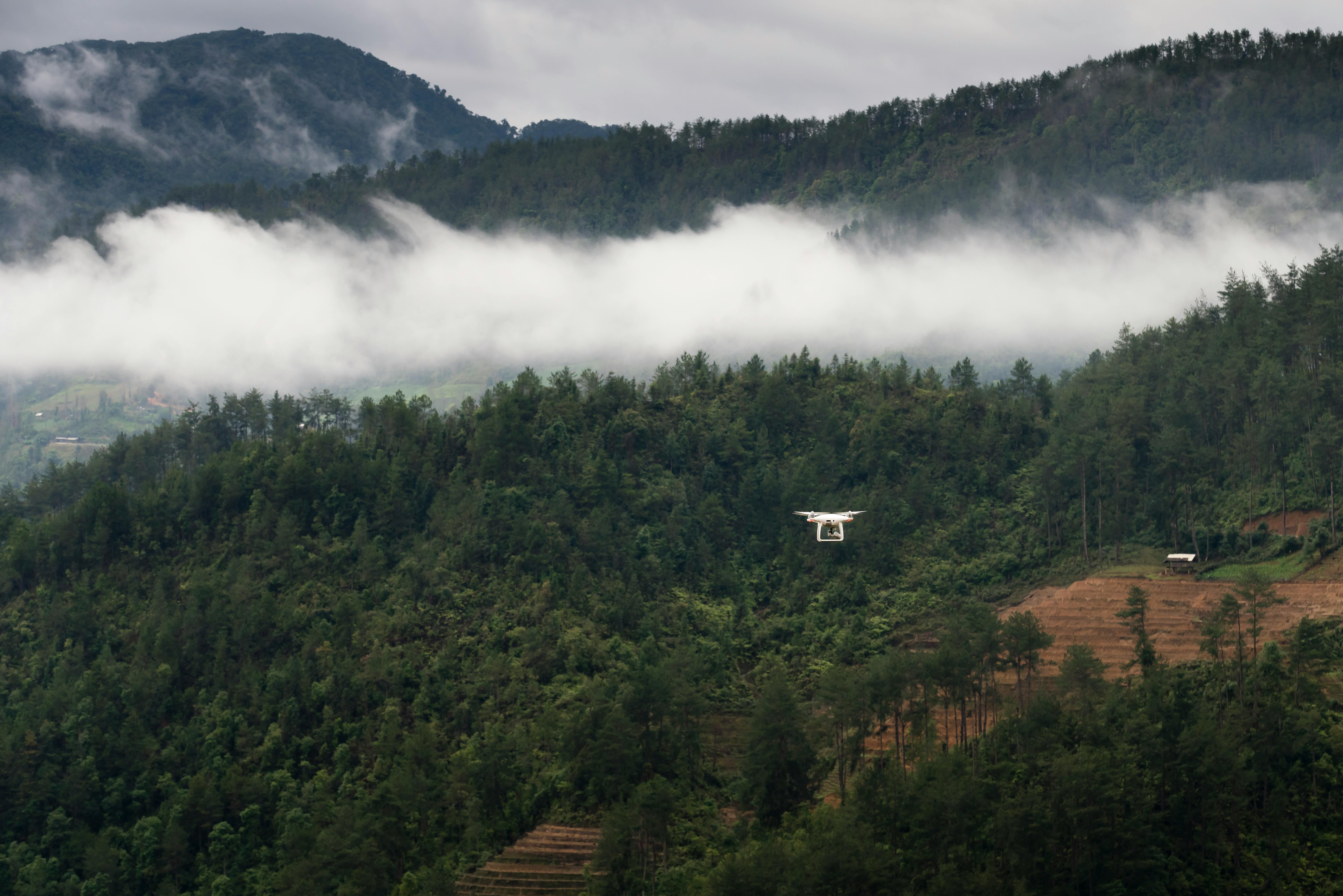 一架无人机飞越云雾缭绕、郁郁葱葱的青山，环境充满冒险气息
