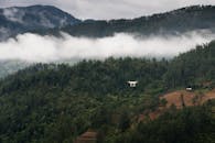 一架无人机飞越云雾缭绕、郁郁葱葱的青山，环境充满冒险气息