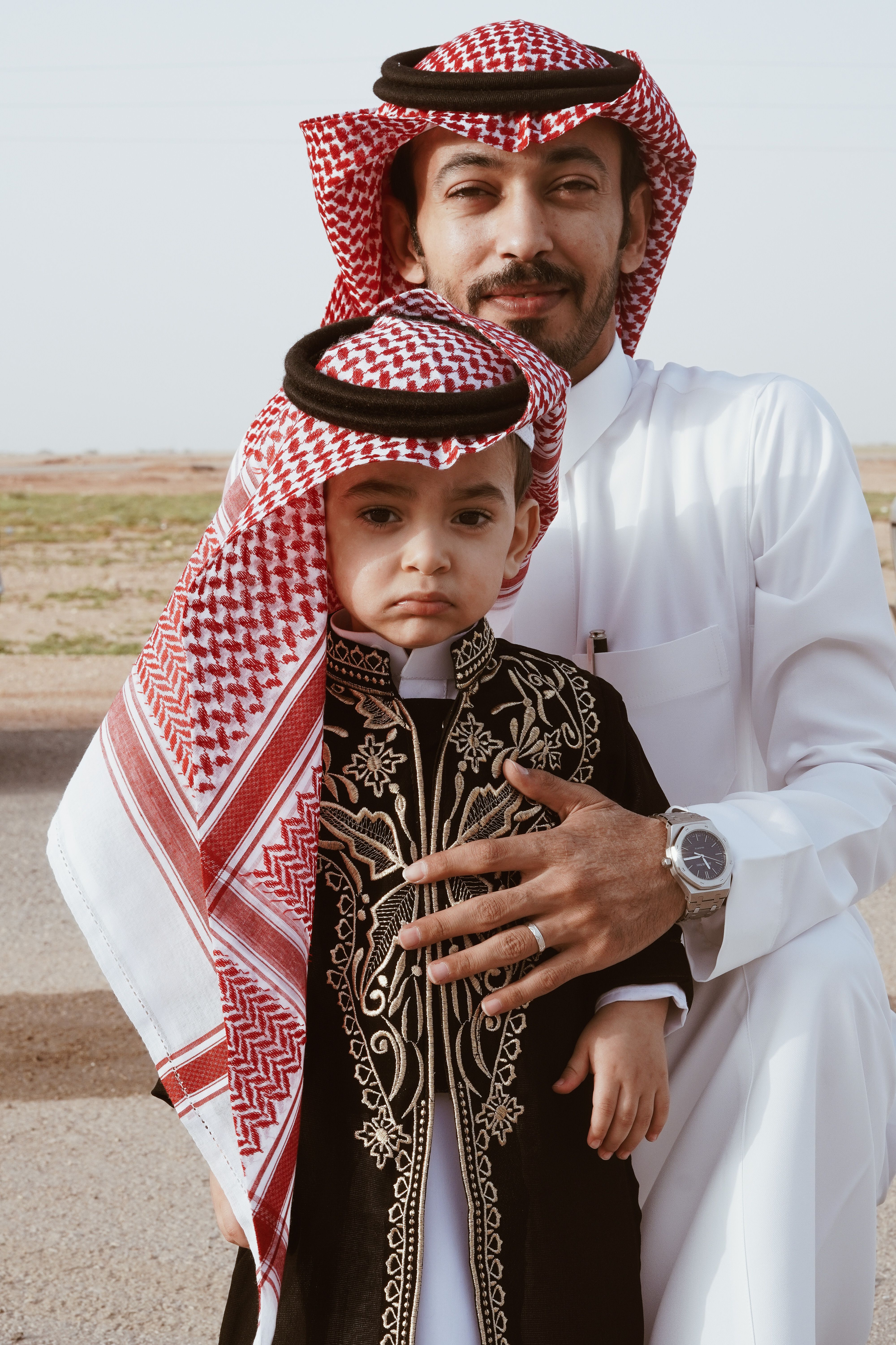 Father and son wearing keffiyeh and traditional attire outdoors.
