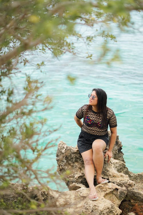 Free A woman sitting on a rock in front of the ocean Stock Photo