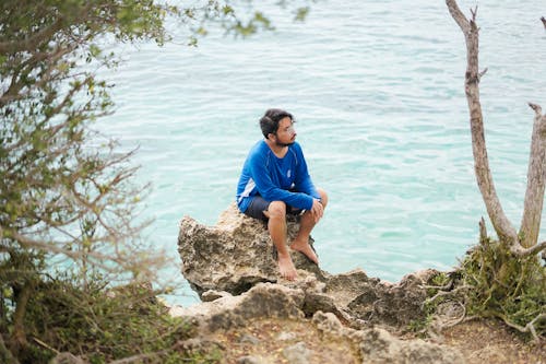 Free A Man Sitting on a Rock on the Shore  Stock Photo