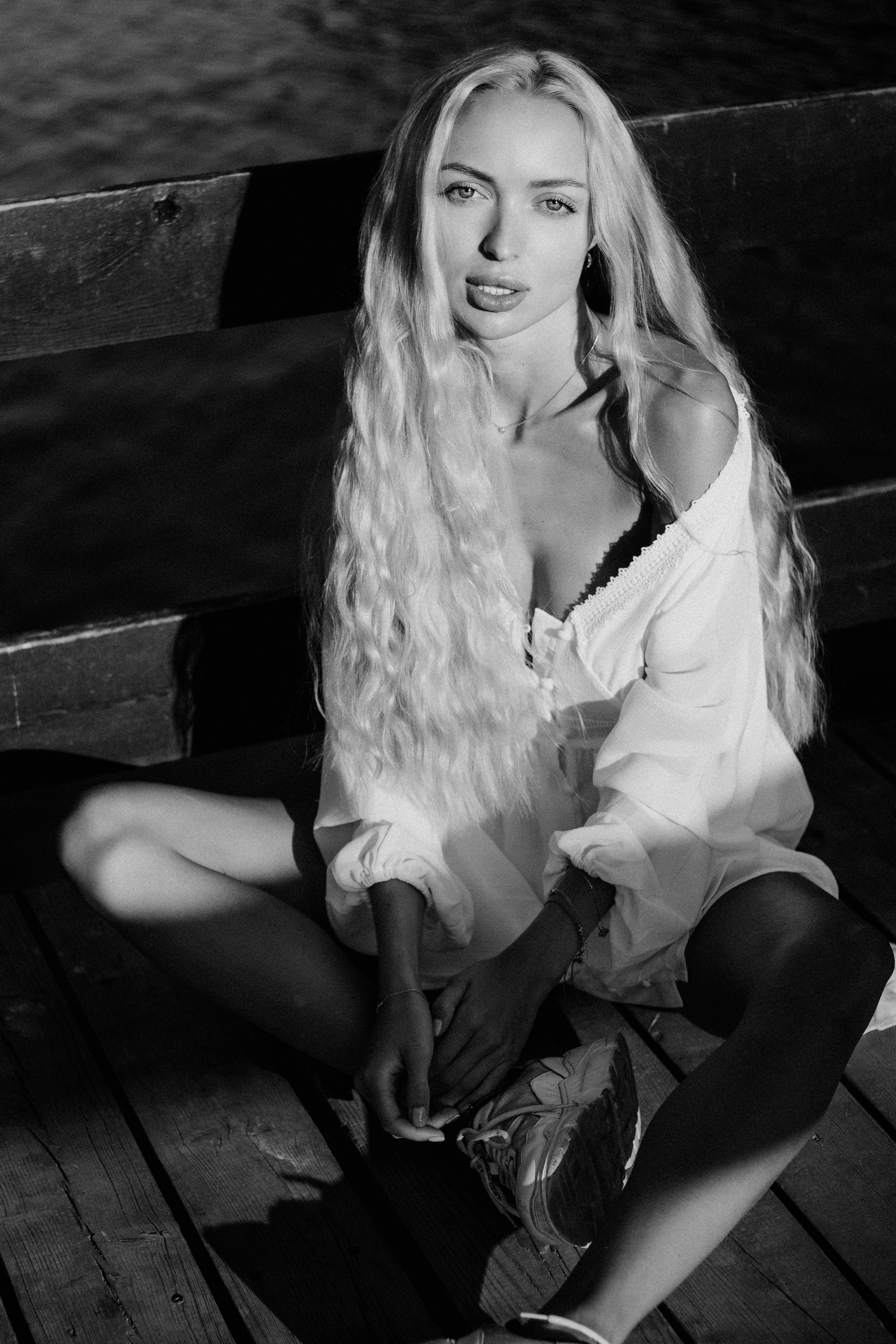 Artistic black and white portrait of a young woman sitting on a pier in the sunlight.