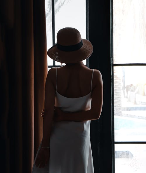 Woman in Dress and Hat Posing near Window