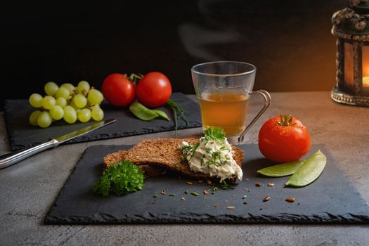 A rustic arrangement of bread, cream cheese, grapes, and herbal tea on a slate platter.