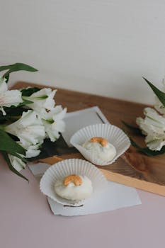 Artistic presentation of white desserts adorned with cashews, surrounded by white flowers.