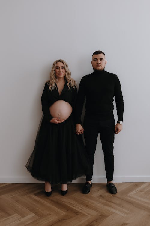Free A pregnant woman and man standing in front of a white wall Stock Photo