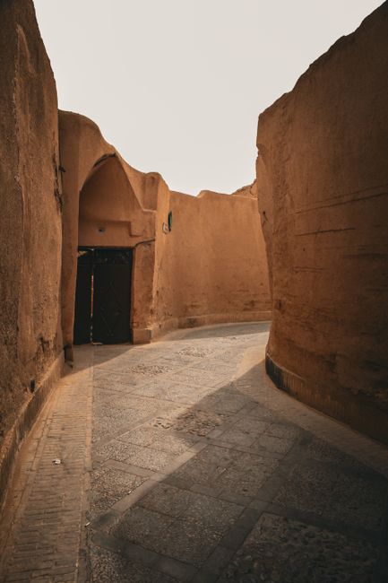 A narrow cobblestone alleyway with dramatic lighting and shadows, featuring ancient earth-toned walls.