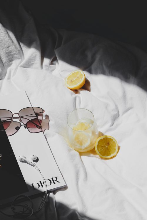 Free Stylish bedside setup featuring sunglasses, a glass of lemonade, and a magazine on white bedding. Stock Photo