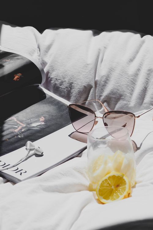 Free Sunglasses and a refreshing lemon drink on soft white linen evoke chic summer vibes, perfect for lifestyle themes. Stock Photo