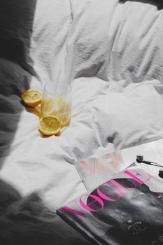A fresh morning setup with a Vogue magazine, lemon slices in a glass, and sunlight on a bed.