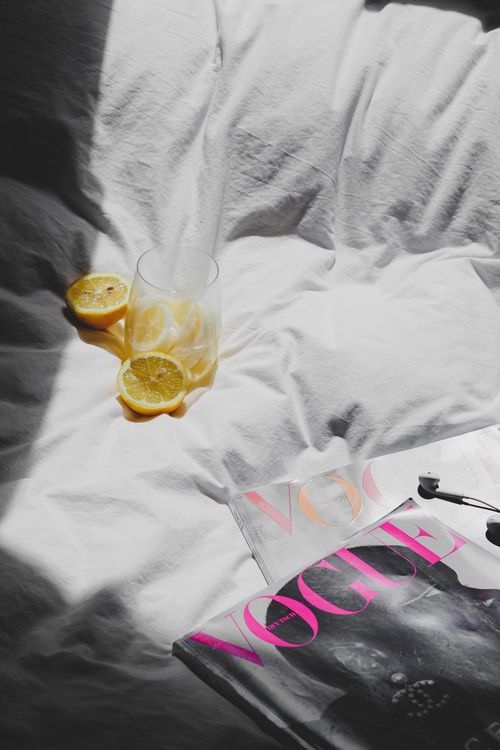 Free A fresh morning setup with a Vogue magazine, lemon slices in a glass, and sunlight on a bed. Stock Photo