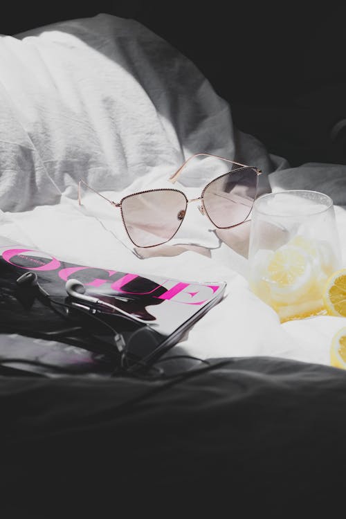 Free A pair of sunglasses and a magazine on a bed Stock Photo