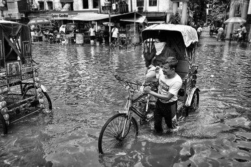Free Black and white image of a man pulling a rickshaw through a flooded street in Kolkata, India. Stock Photo