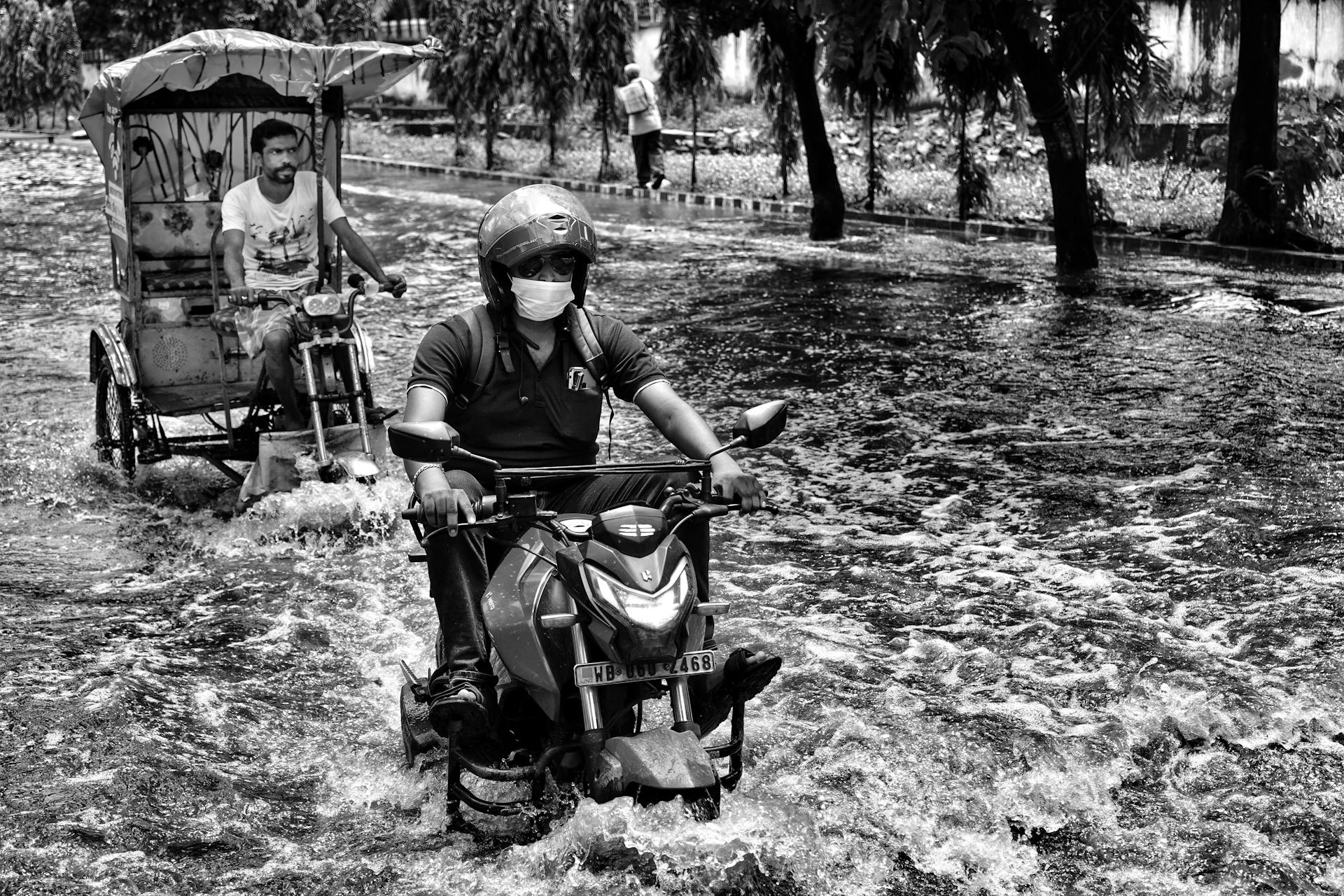 A man rides a motorbike through flooded streets in Kolkata, India, showcasing urban flooding challenges.