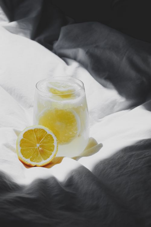 Free Glass of lemon water placed on a bed with bright sunlight. Perfect for wellness concepts. Stock Photo