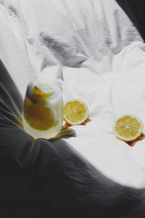 Free Glass of lemon water on sunlit bedding offering a refreshing citrus drink vibe. Stock Photo