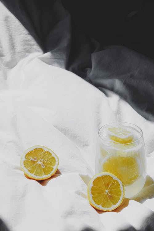 A glass of lemonade and two slices of lemon on a bed