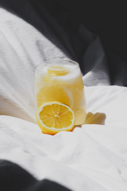 Free A glass of lemon-infused water placed on a sunlit bedspread, capturing a bright, refreshing moment. Stock Photo