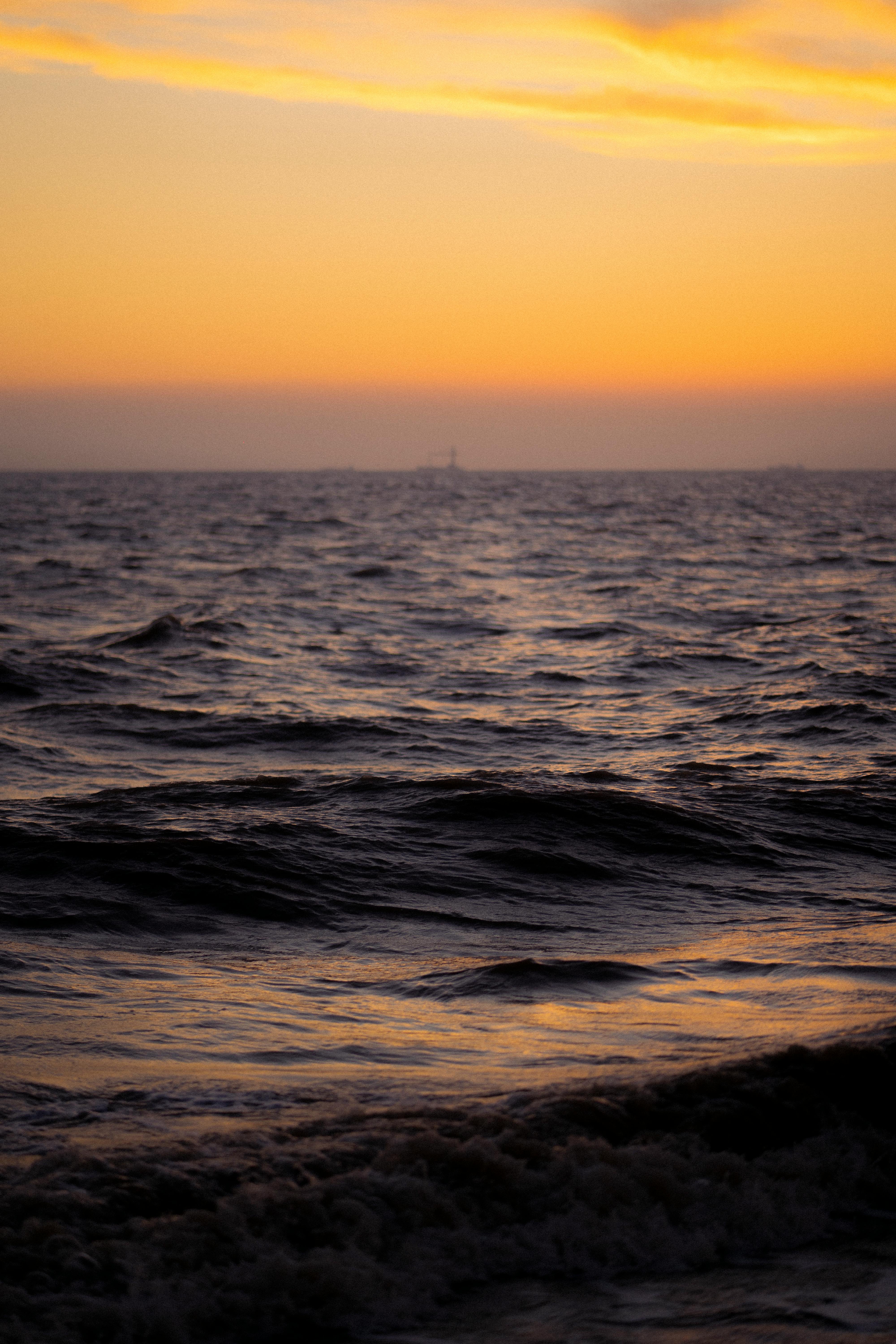 Calm waves and orange sunset reflecting over the ocean horizon.