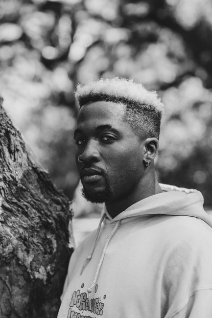 Striking black and white portrait of a man outdoors against tree bark.
