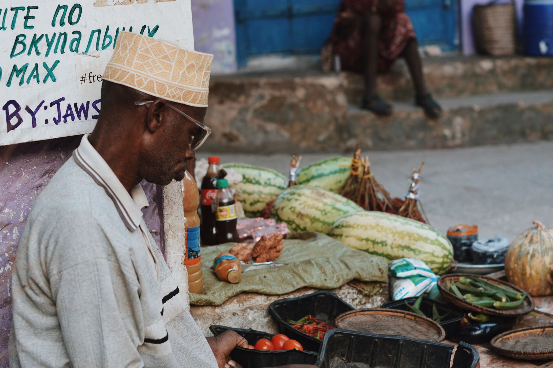 A market scene in Zanzibar City featuring a vendor with fresh produce like tomatoes, watermelons, and spices.
