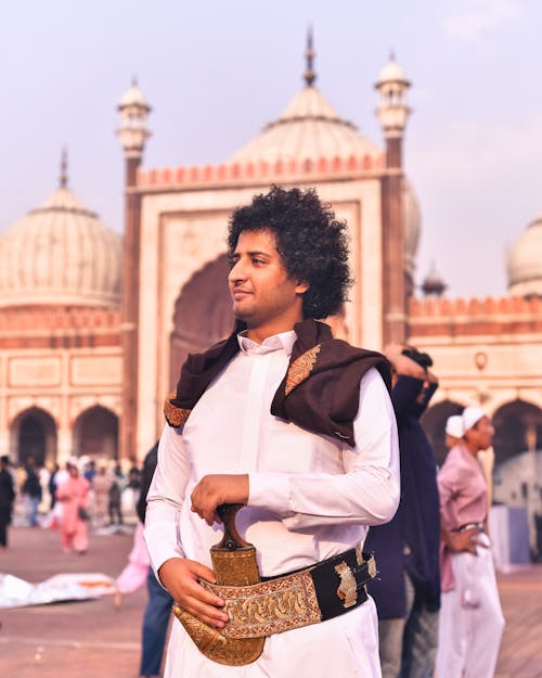 A man in traditional clothing is standing in front of a mosque