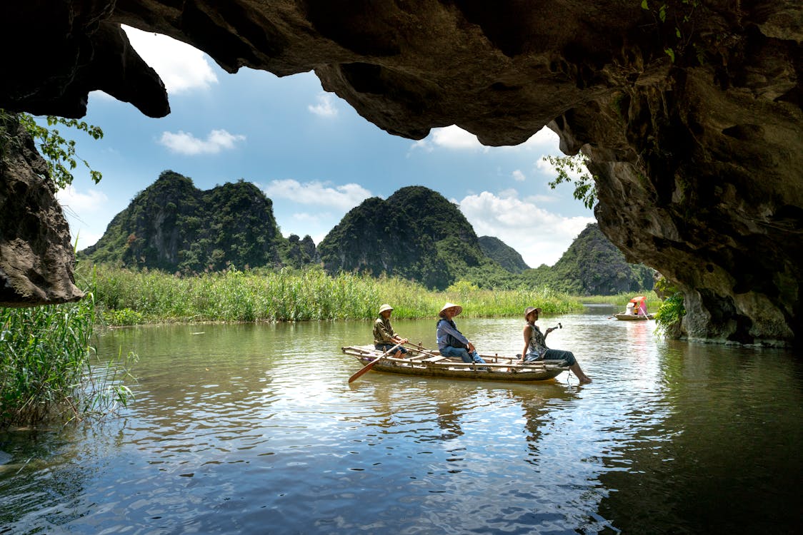Three People Sitting on Boat While Sailing Under Cave