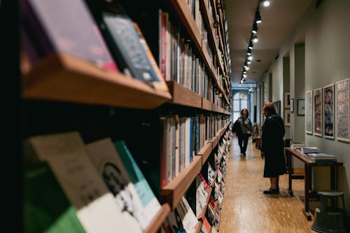 A woman walking down a long aisle in a bookstore