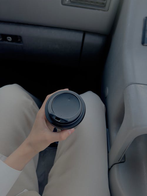 A person holding a coffee cup in the back seat of a car