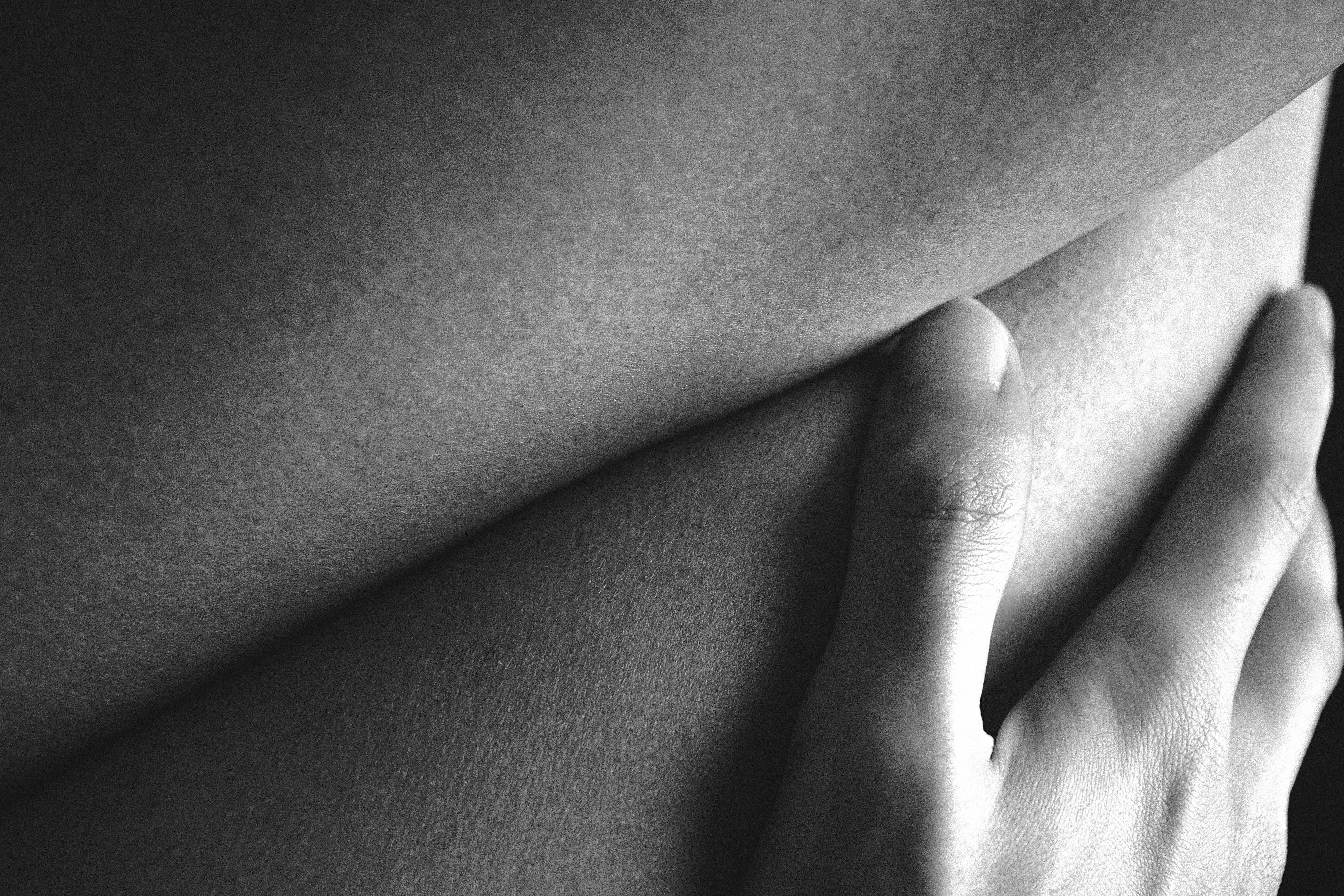 Close-up of gentle hand touching smooth bare skin intimately, evoking tender erotic connection in dim light