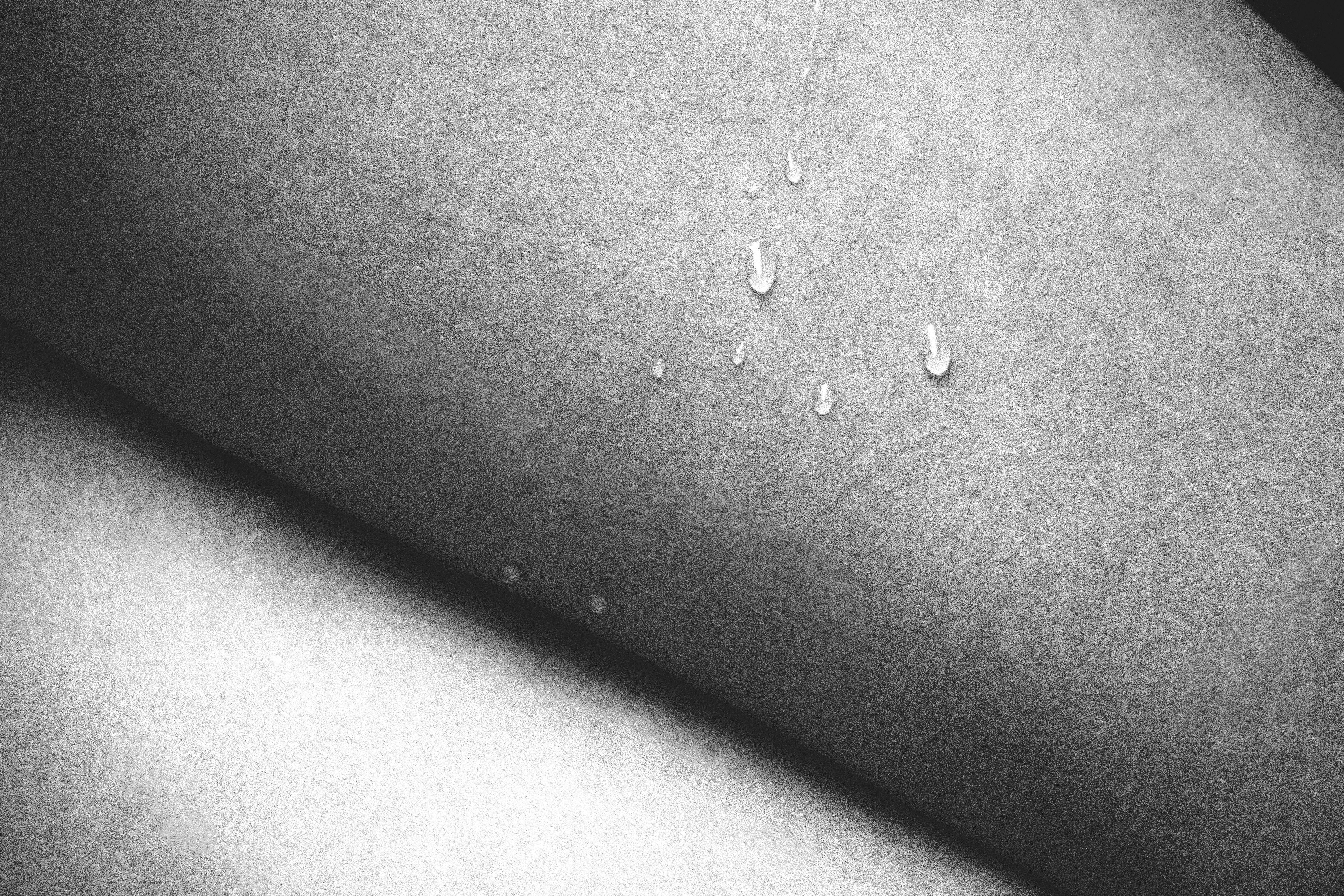 A conceptual black and white close-up photo of skin with water drops, highlighting texture and contrast.