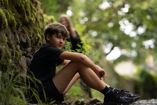 A boy sitting on the ground next to a tree