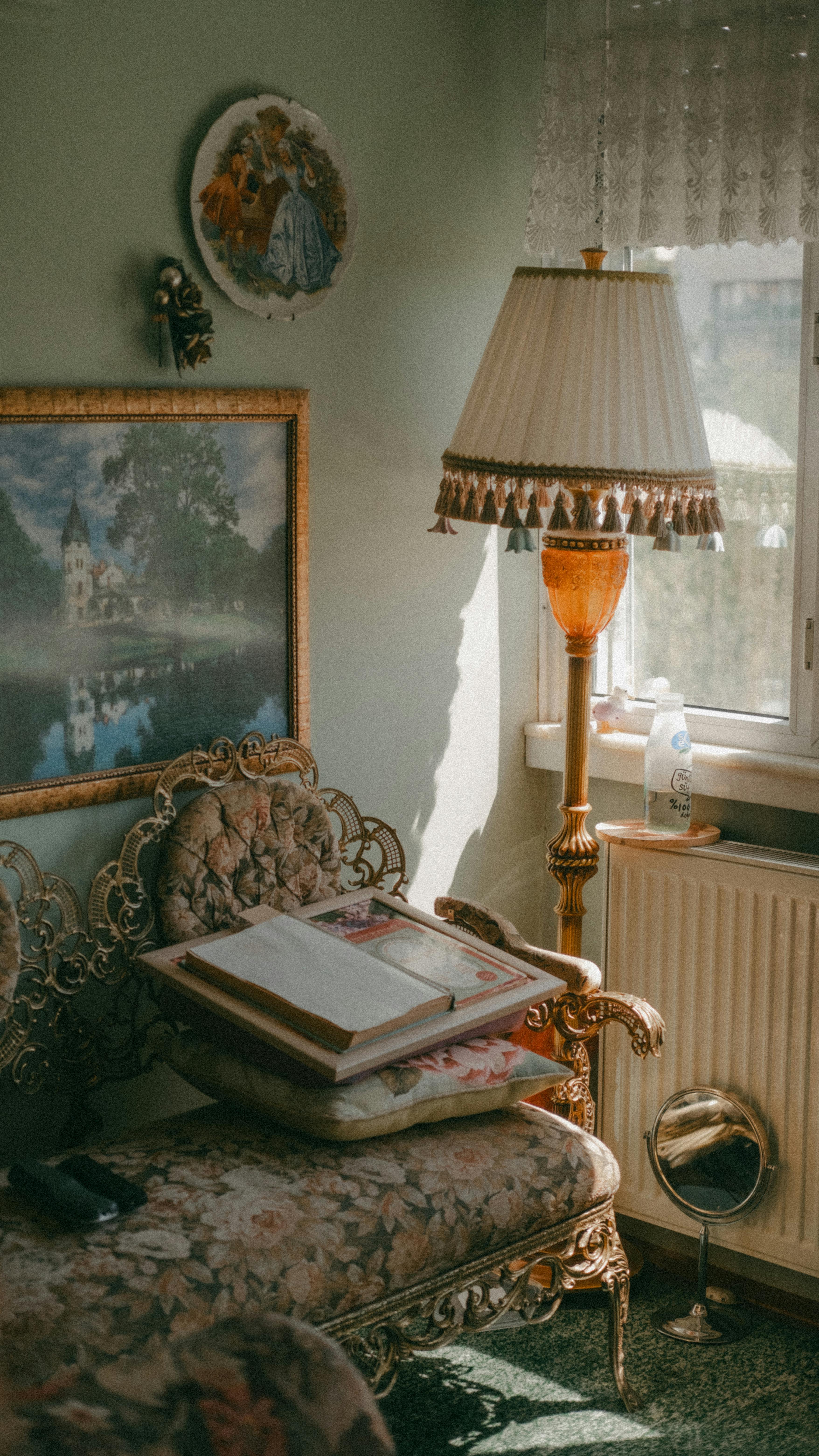 A cozy vintage living room with ornate furniture, artwork, and a floor lamp by a window.
