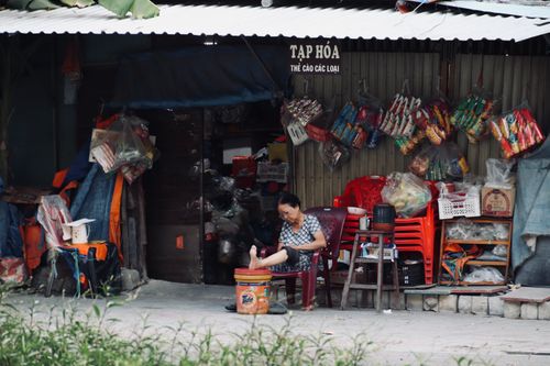 Free A woman sitting outside a rural Vietnamese store surrounded by various goods and colorful items. Stock Photo