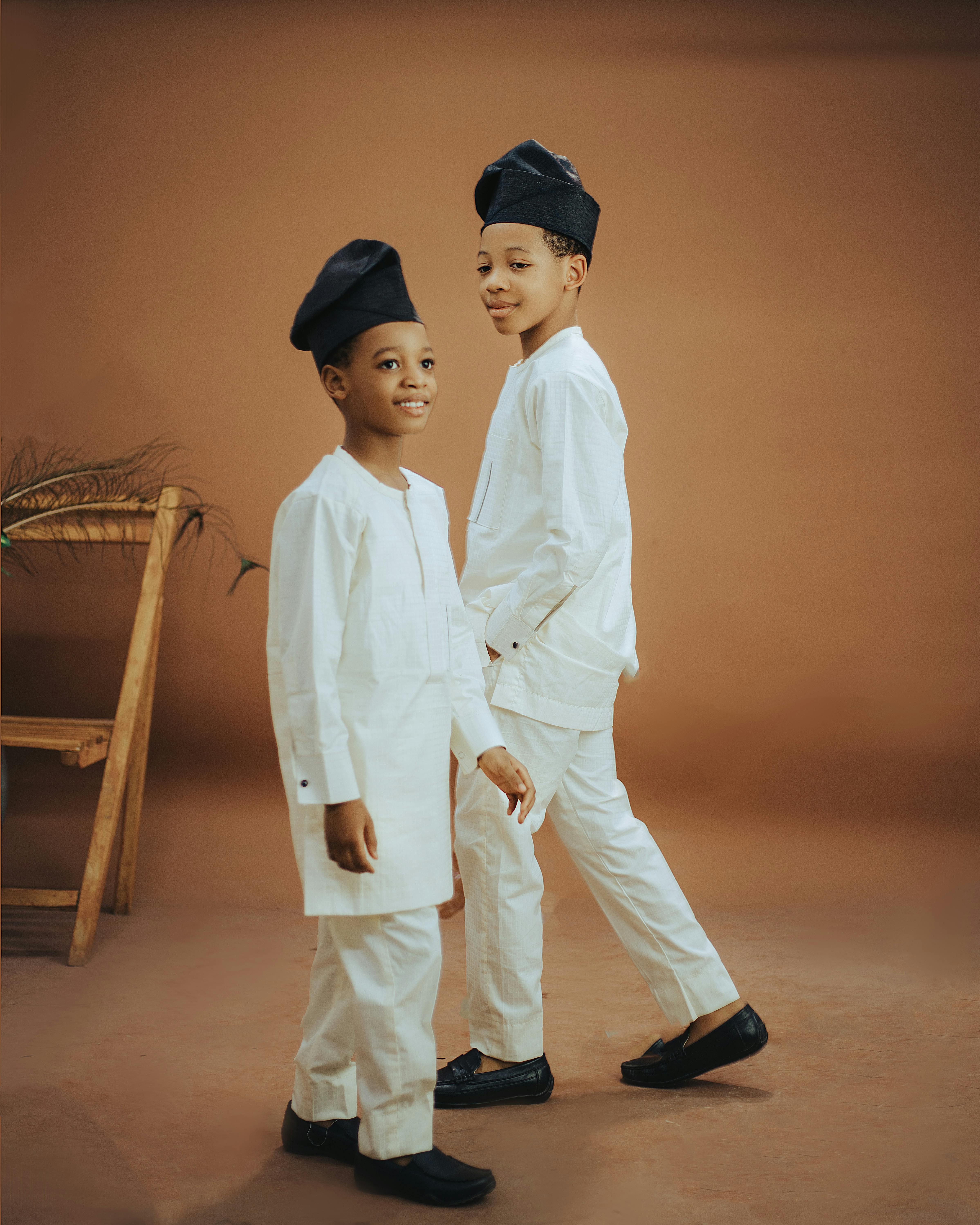 Free Two young boys smiling in traditional white attire with black hats in a studio setting. Stock Photo