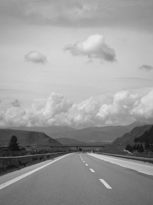 A black and white photo of a highway with clouds