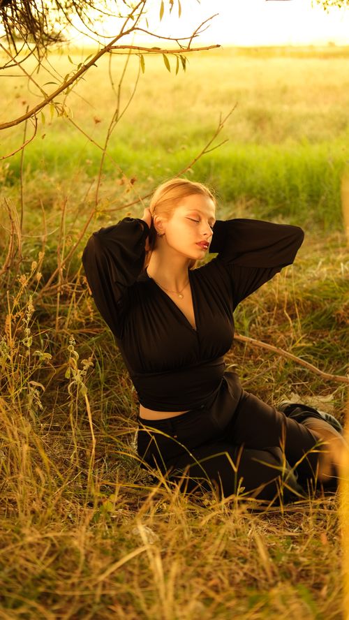 Free Elegant woman in black dress poses gracefully in a sunlit meadow, enveloped in nature's tranquility. Stock Photo