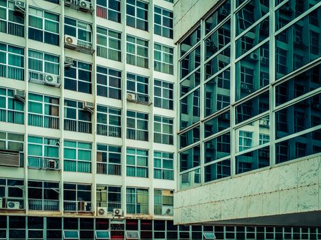 Converging urban buildings with reflective glass and numerous windows seen from below.