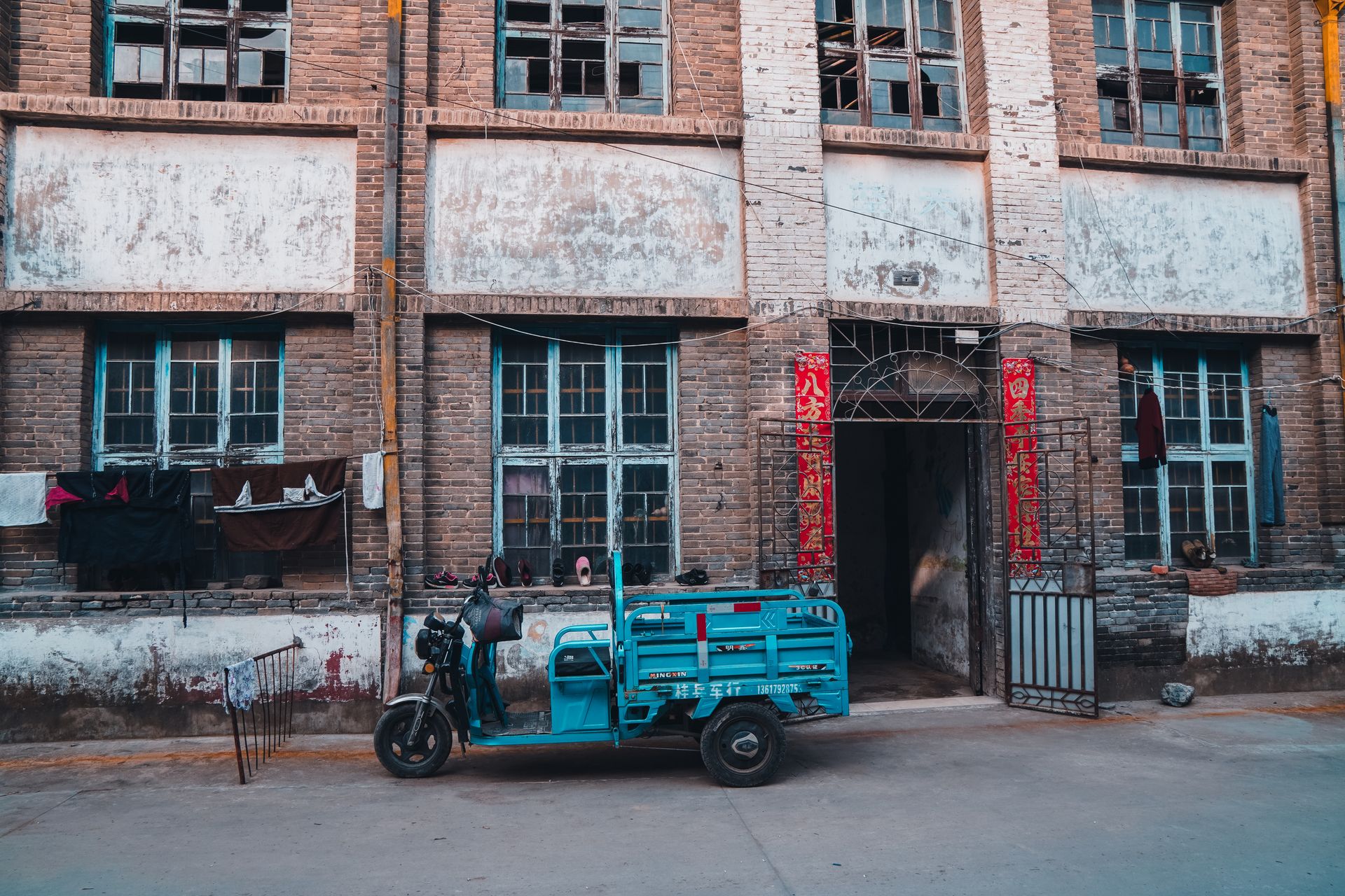 Blue auto rickshaw parked by an old brick building with laundry and Chinese decorations in Jiangxi, China.