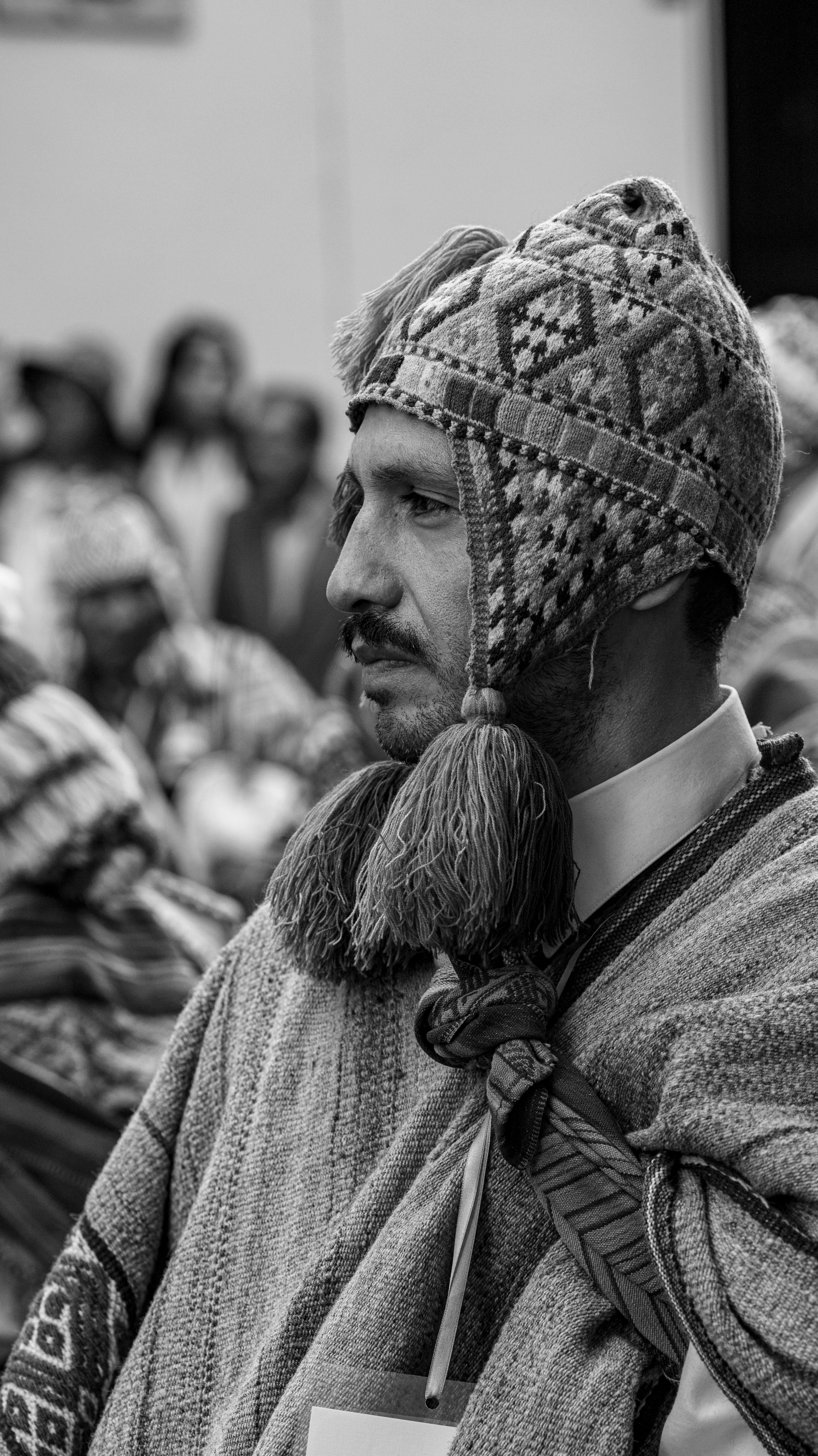 Black and white portrait of a man wearing traditional Andean clothing, captured outdoors.