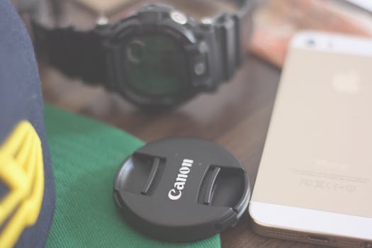 A stylish flat lay of a smartphone, watch, and camera lens cap on a table.