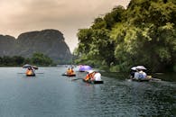 人们在平静的河面上乘船游览，四周绿树环绕，远山如黛，尽享宁静