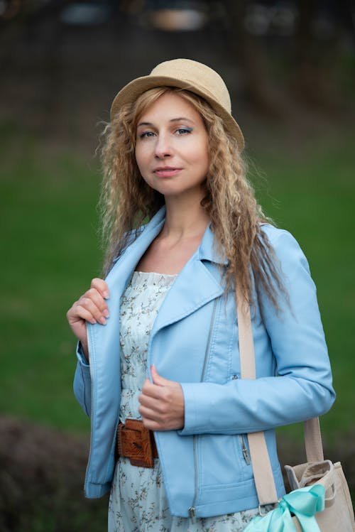 A woman in a hat and blue jacket holding a purse