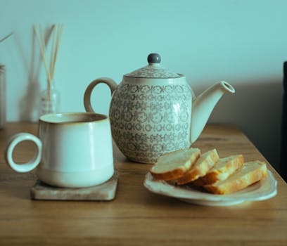 Warm still life of a teapot and mug with sliced bread on a wooden table.