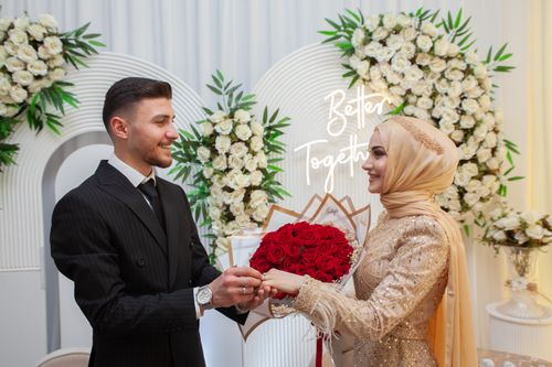 Free A stylish wedding portrait of a joyful couple exchanging rings with a beautiful floral backdrop. Stock Photo