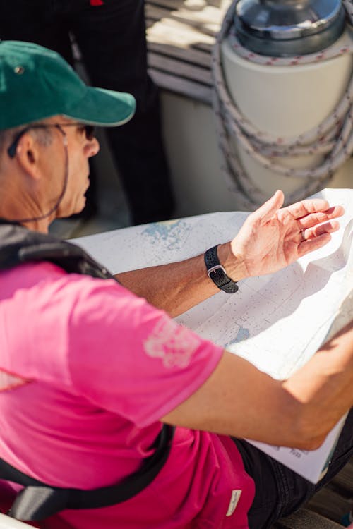 A man in a pink shirt and green hat is looking at a map