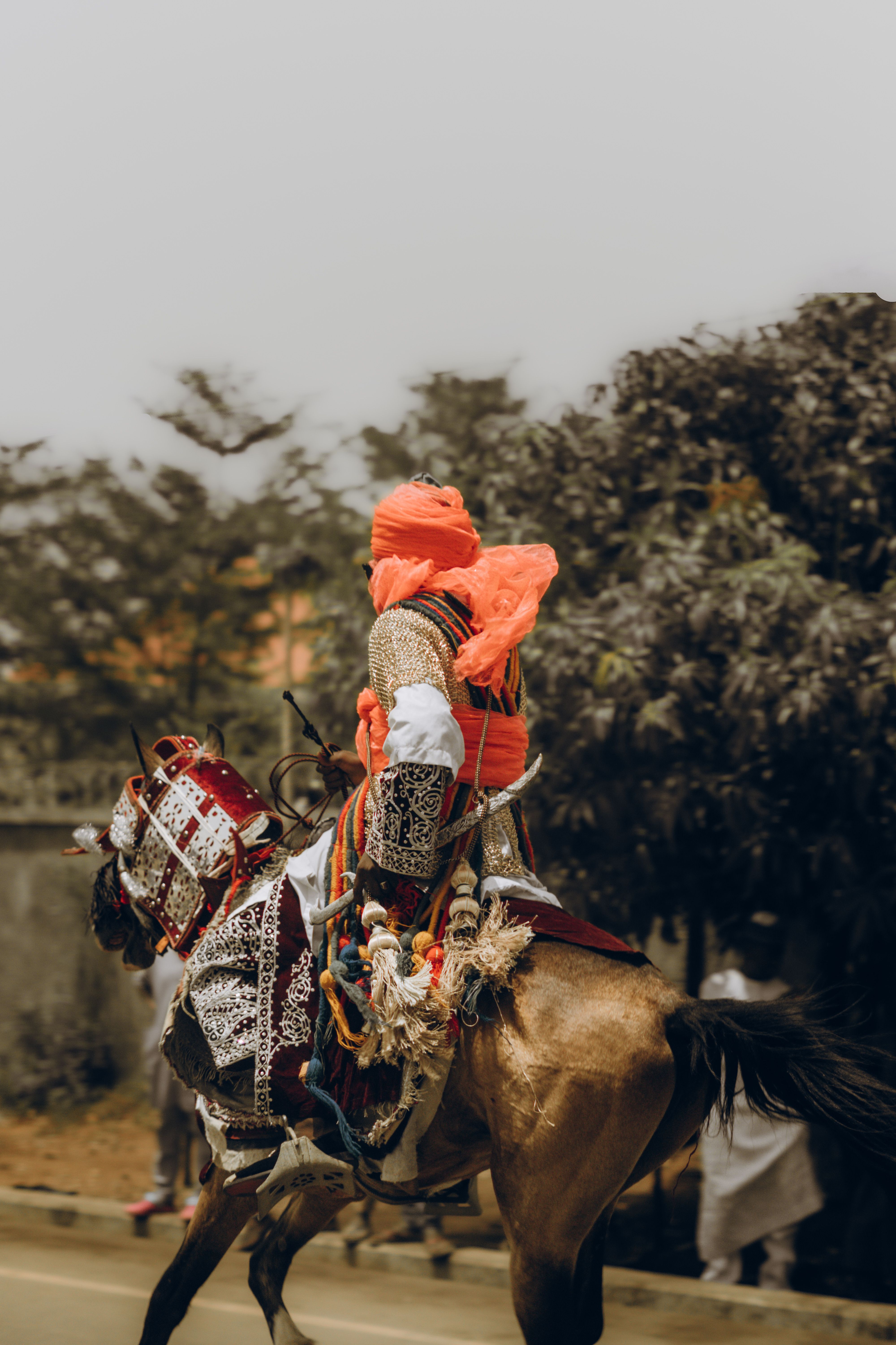 A man in traditional attire rides an ornamented horse during a parade outdoors, showcasing cultural heritage.