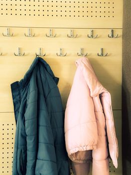 Two winter coats hanging on wall hooks, perfect for fashion displays.